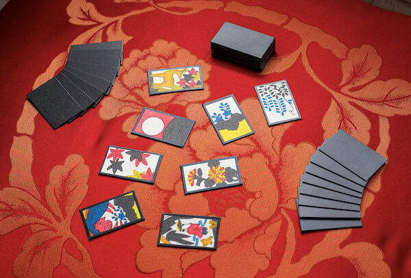 Two hands of Hanafuda cards face down on a table with eight cards dealt face-up between them and the remainder of the cards in a stack face-down to the side.