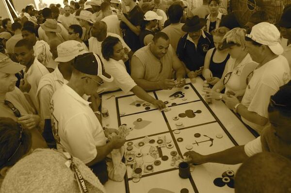 A Crown & Anchor table scattered with money and weights and surrounded by a large crowd.