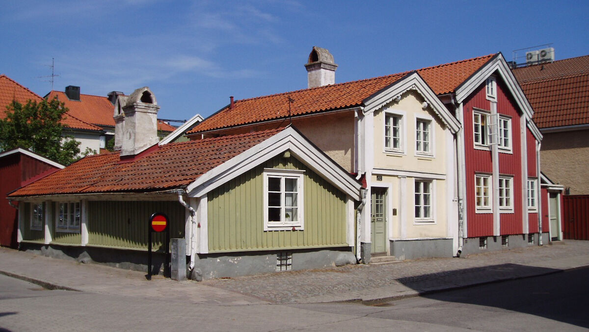 Three houses, from left to right a small olive coloured house, a larger off-white house, and then the tallest, a red house.