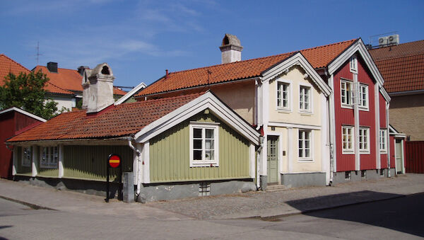 Three houses, from left to right a small olive coloured house, a larger off-white house, and then the tallest, a red house.