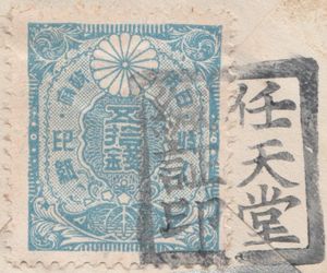 A square blue tax stamp reading â€˜50 senâ€™ in Japanese with a stylized chrysanthemum flower. The stamp is overprinted with black ink reading â€˜Nintendoâ€™ in Japanese.