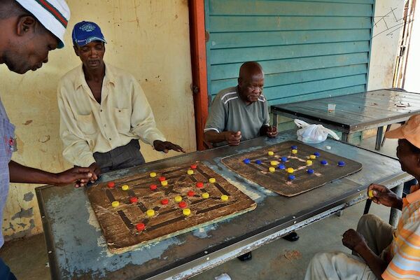 Two sets of men playing on two different morabaraba boards.