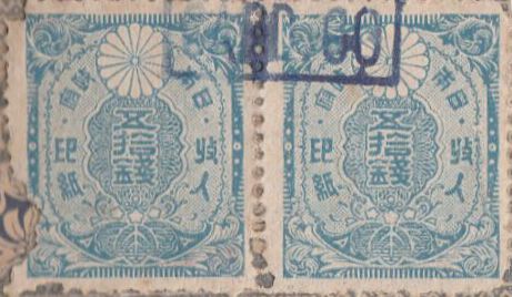 A square blue stamp reading â€˜50 senâ€™ in Japanese with a stylized chrysanthemum flower.