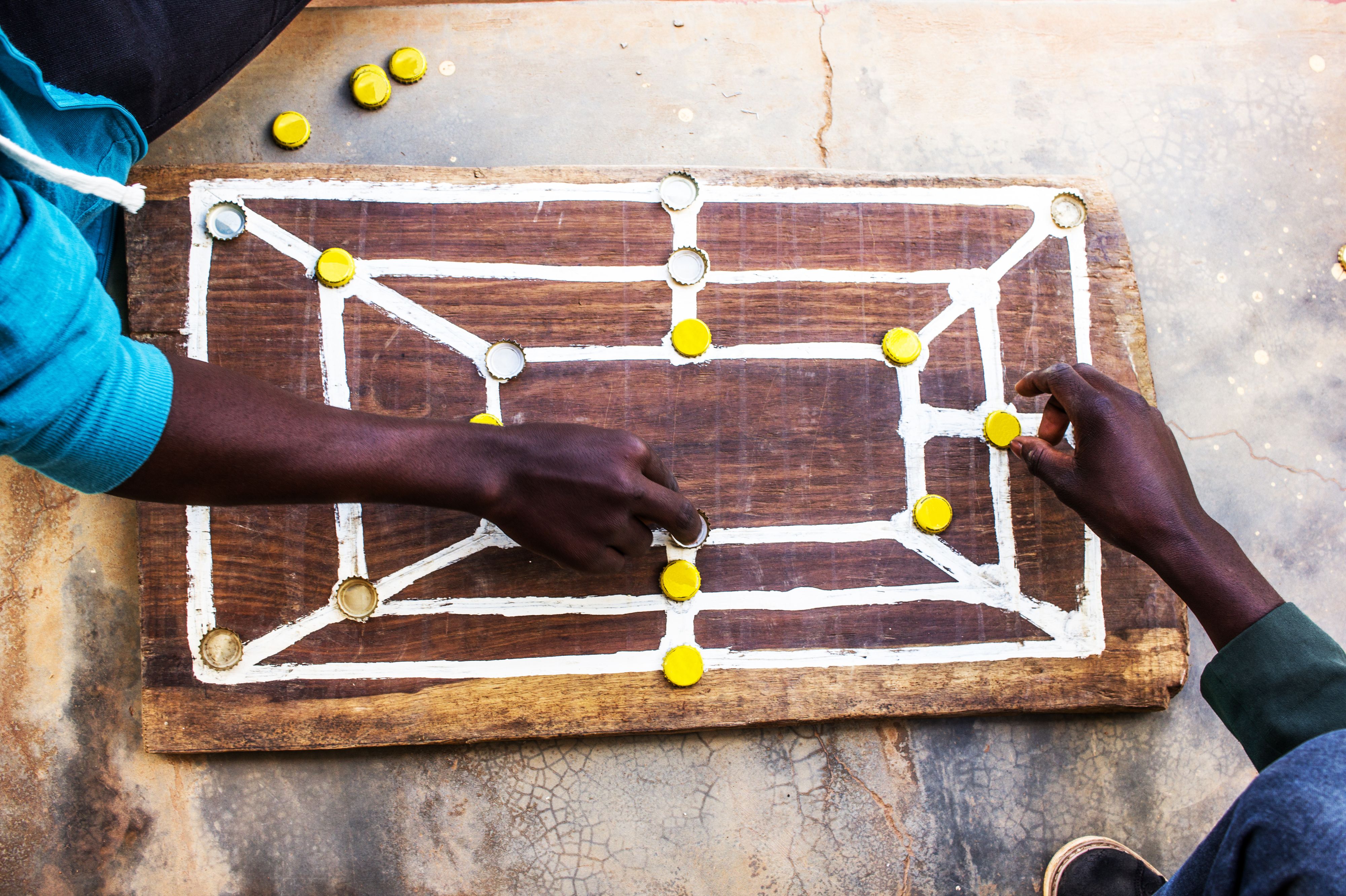 A morabaraba board with bottlecaps being used as pieces. One player is using them right-side-up and the other player is using them upside-down.