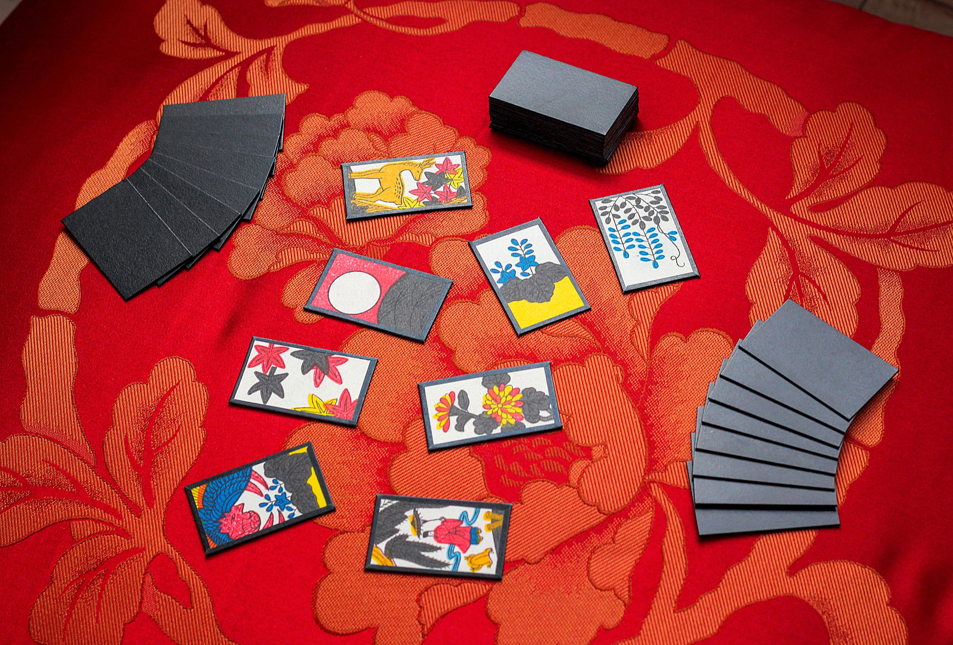 Two hands of Hanafuda cards face down on a table with eight cards dealt face-up between them and the remainder of the cards in a stack face-down to the side.