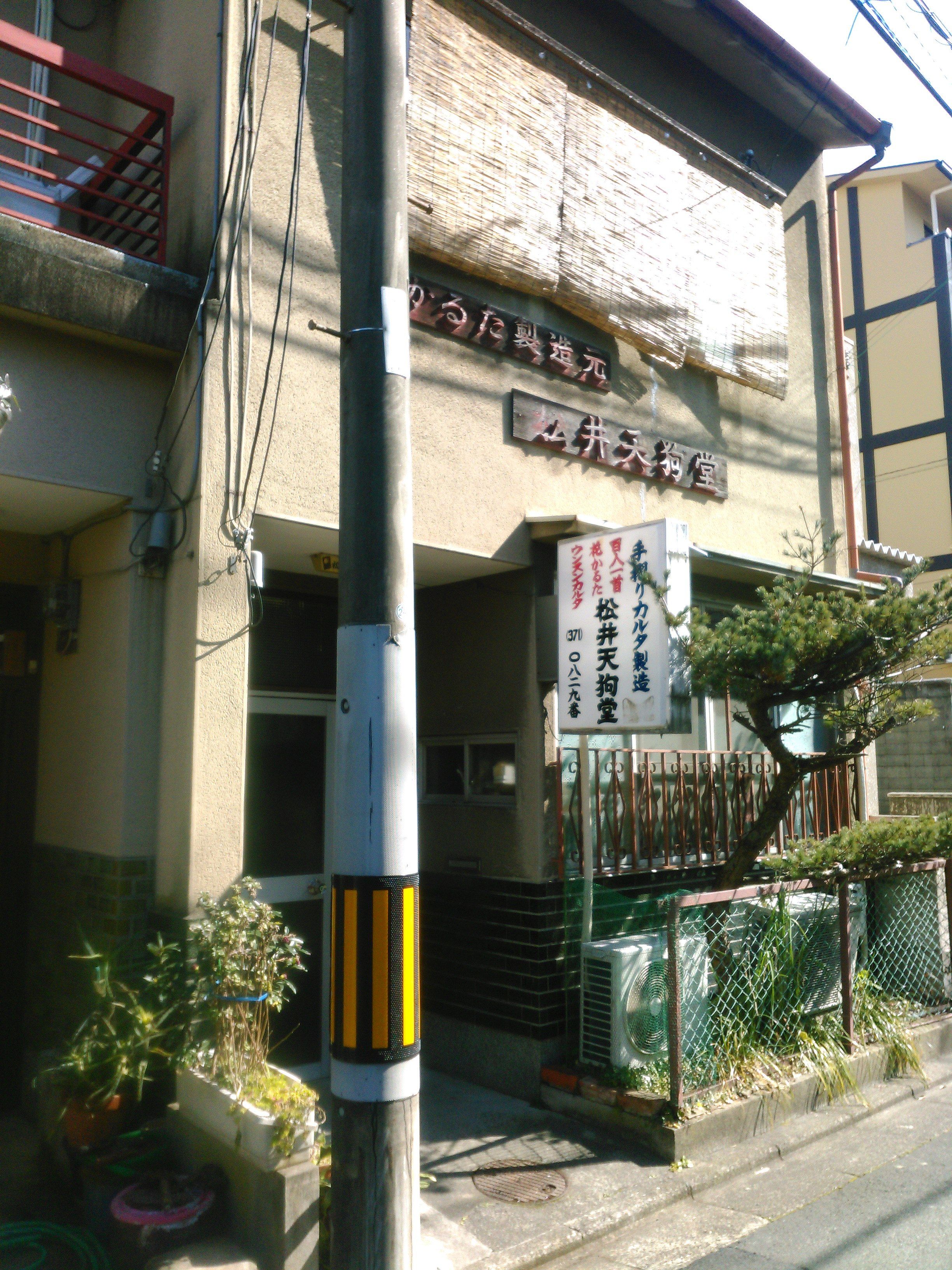A Japanese storefront with disintegrating sign and a pine tree growing in front.