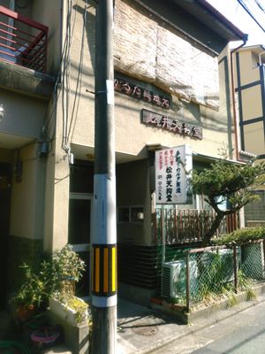 A Japanese storefront with disintegrating sign and a pine tree growing in front.