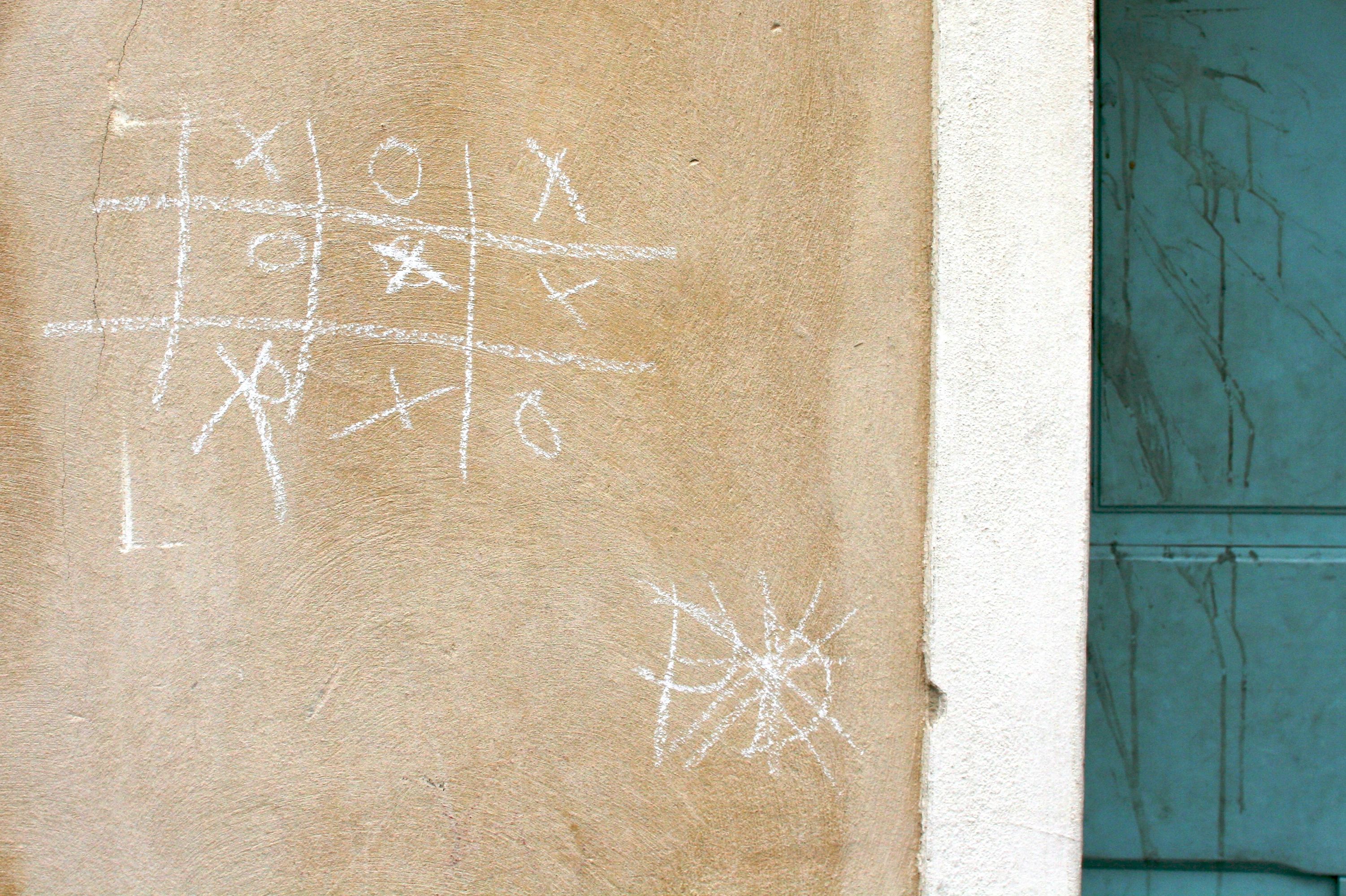 A wall with a completed tic-tac-toe game drawn on it in chalk.