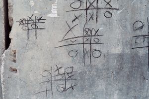 Several games of tic-tac-toe scrawled on a concrete wall.