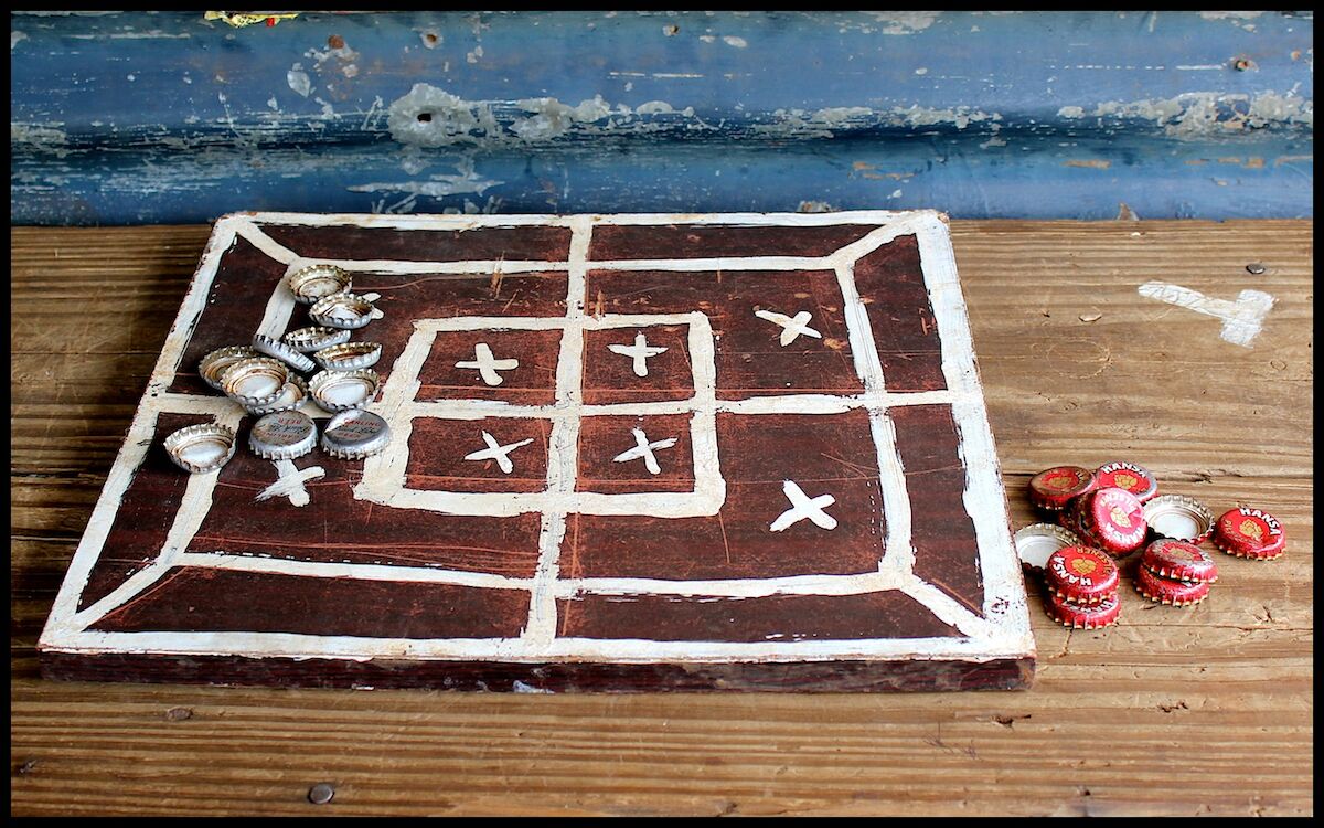 A well-used morabaraba board with two different types of bottle caps for pieces.