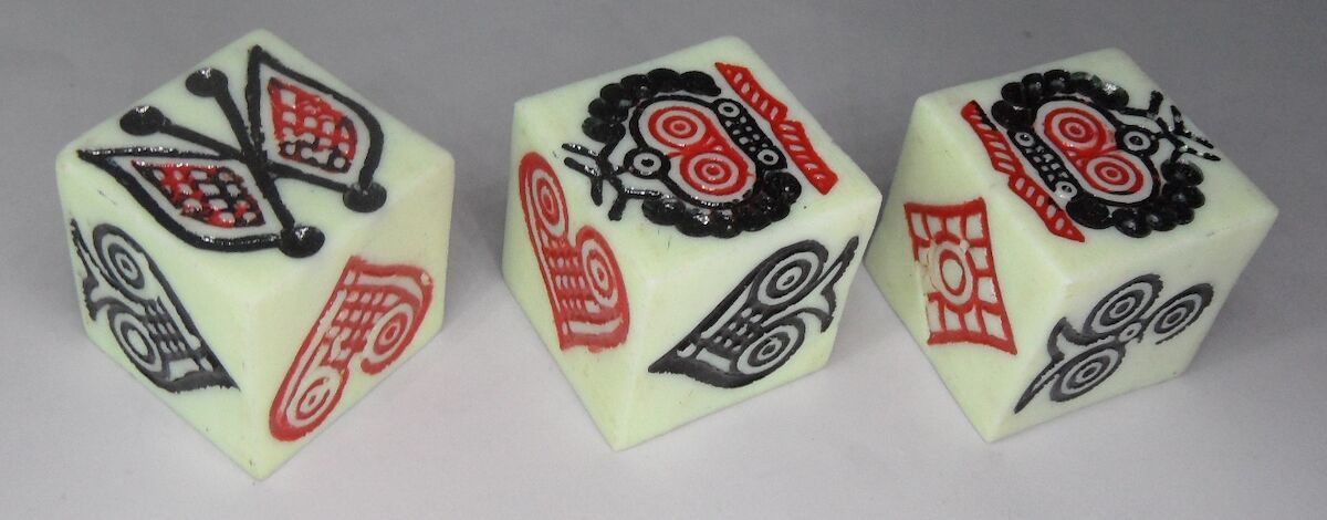 Three dice bearing the symbols of the flag, crown, and playing card symbols, in elaborate carvings.