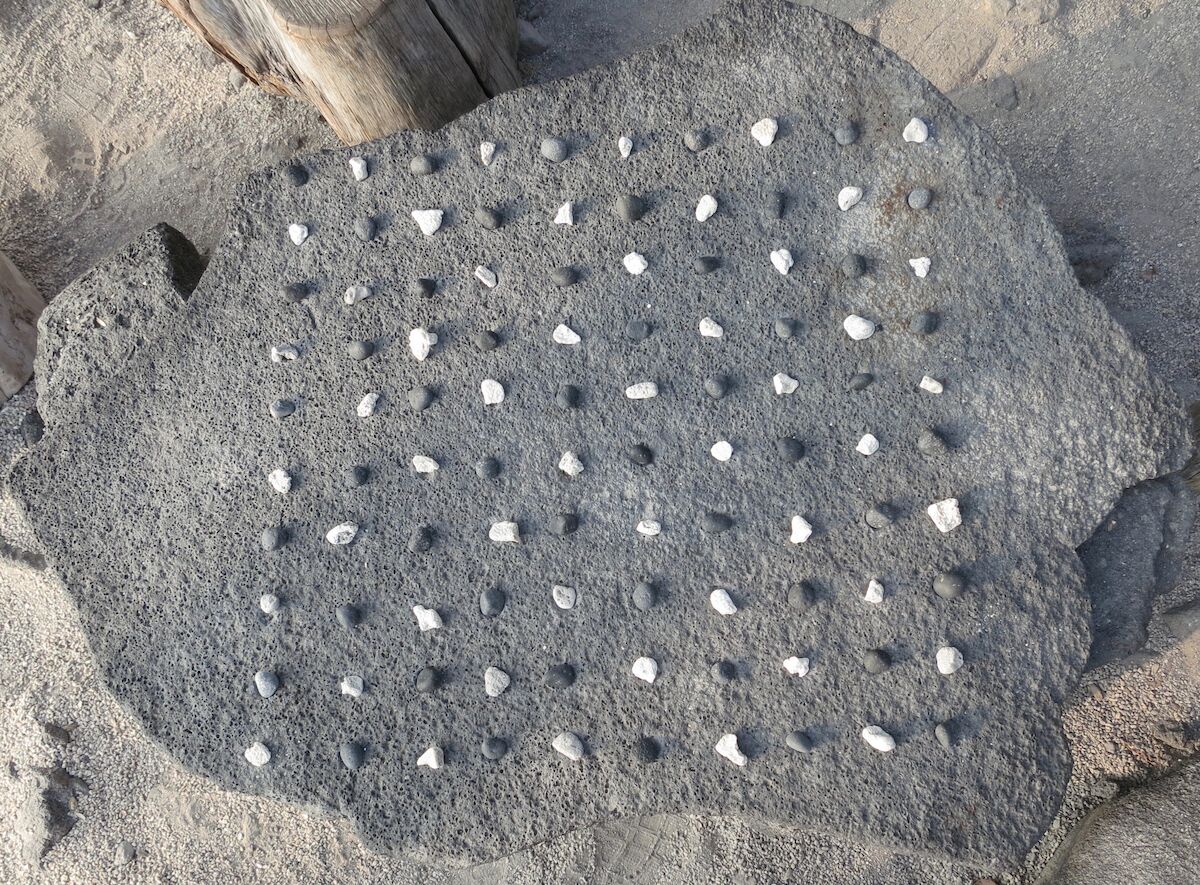 A kōnane board set up for play with pieces in a checkerboard pattern.