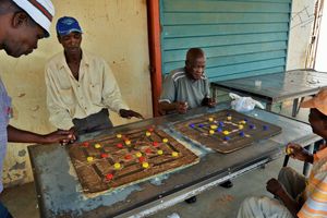 Two sets of men playing on two different morabaraba boards.