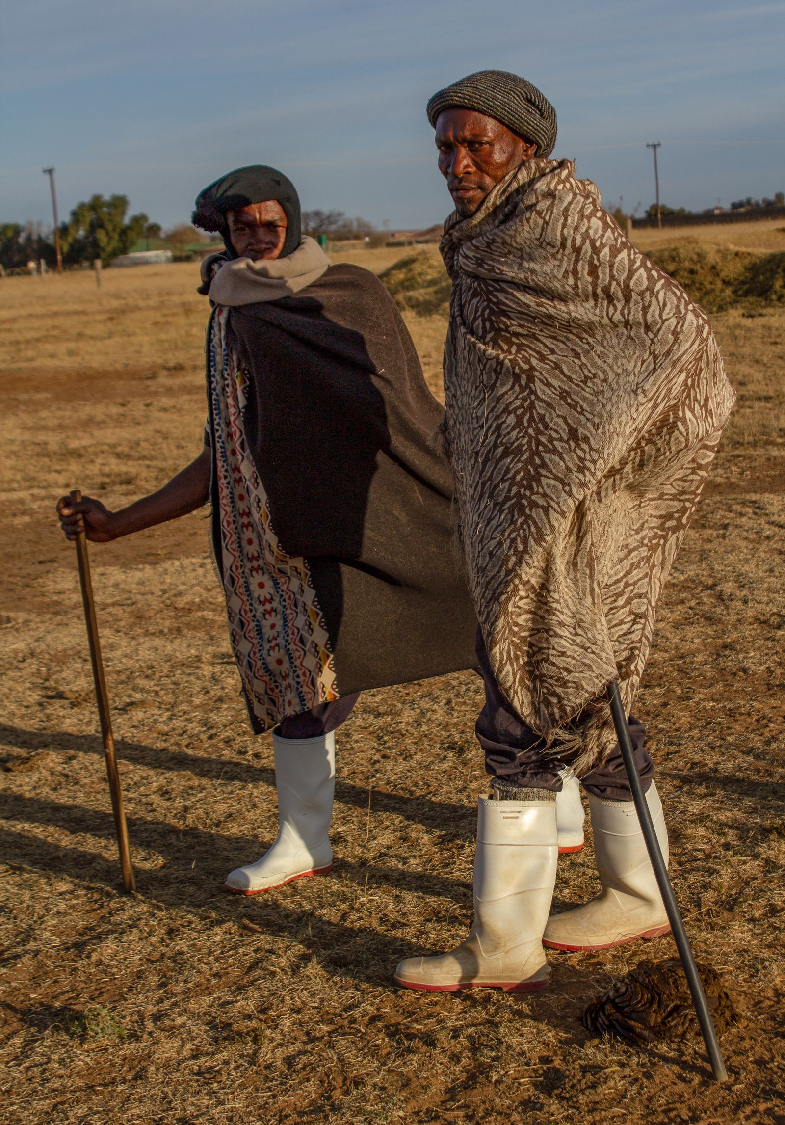 Two men dressed in warm blankets, gumboots, and balaclava, carrying staffs